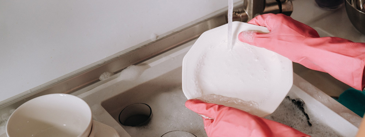 girl pink gloves washes dishes by hand sink