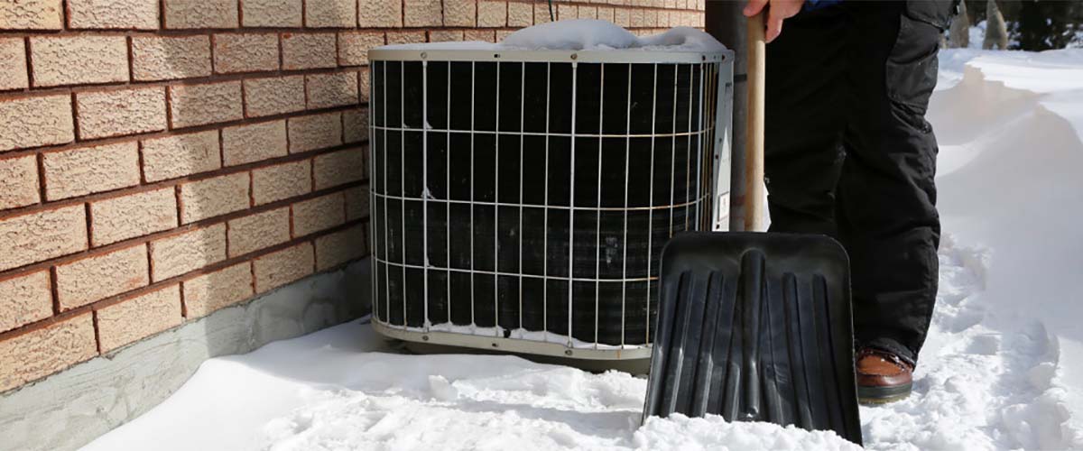 ac unit in snow outside man shoveling